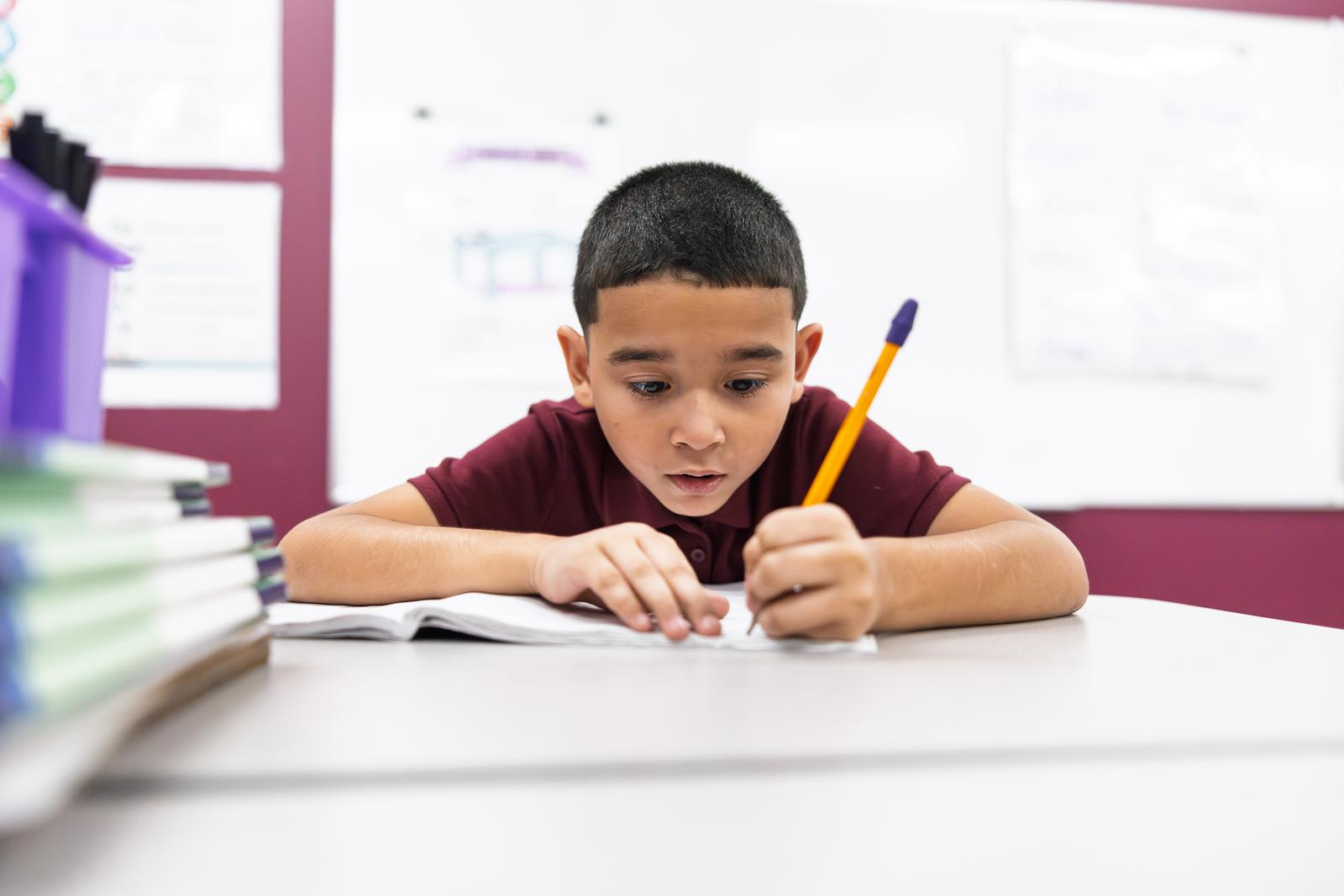 A student writing intently at his desk in a classroom